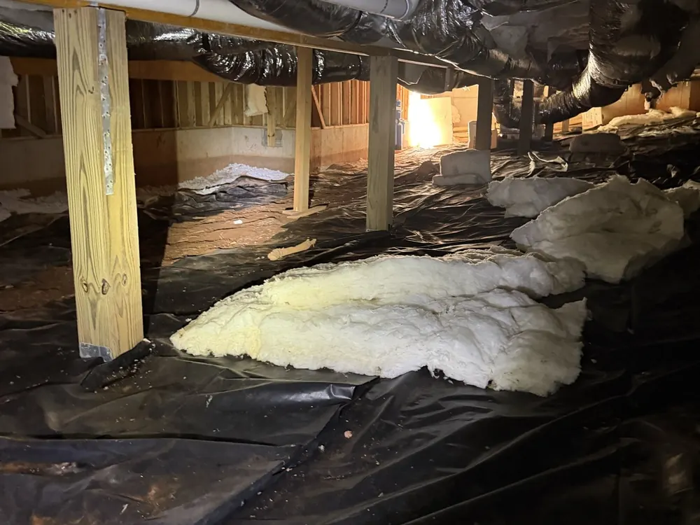 Loose insulation and worn plastic across a crawl space floor before the work