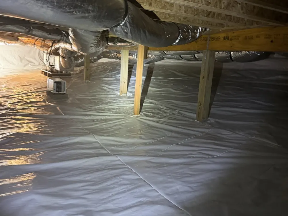 A sealed crawl space with a white liner across the floor and up to the ductwork