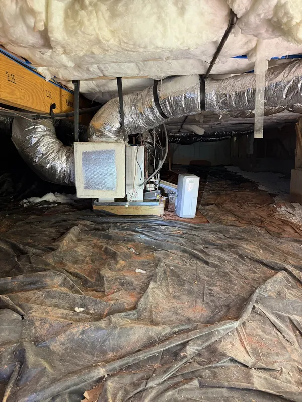 Before: an air handler hanging over torn black plastic and bare red clay in a crawl space, from one of our jobs