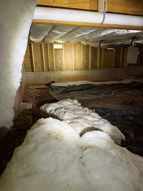 Long runs of insulation lying on black plastic under the floor framing